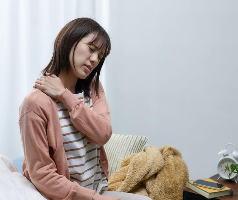 woman holding shoulder in pain at home showing neck pain and need for massage